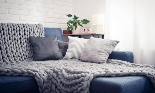 Gray knitted blanket from merino wool on couch with pillows in the interior of the living room